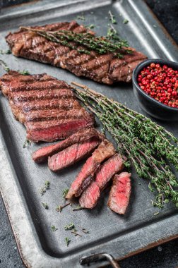 BBQ roast denver top blade beef meat steak on a steel tray with herbs. Black background. Top view.