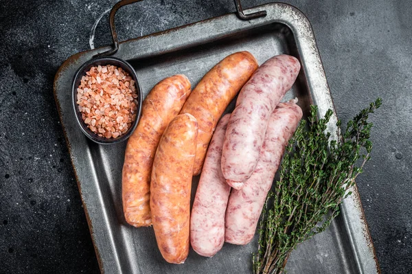 Raw barbecue sausages with spices in kitchen tray. Black background. Top view.