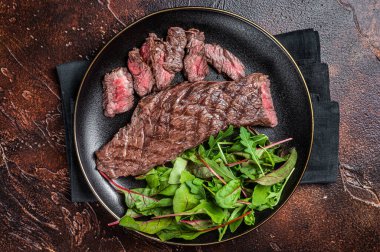 Juicy Grilled Machete skirt beef meat steak on plate with salad. Dark background. Top view.