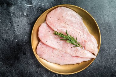 Uncooked Raw chicken chop breast fillets on a plate, poultry meat. Black background. Top view.