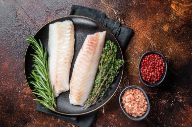 Raw cod loin fillet steaks with herbs on plate. Dark background. Top view.