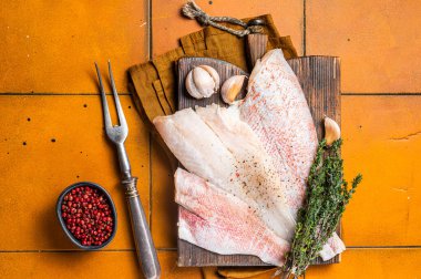 Uncooked ocean red perch fillet, redfish with herbs and spices. Orange background. Top view.