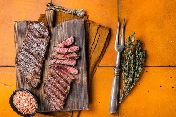 BBQ grilled denver top blade beef meat steak with thyme on a wooden board. Orange background. Top view.