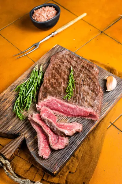 BBQ dry aged wagyu Flank Steak on a cutting board. Orange background. Top view.