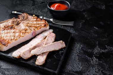 Grilled slised pork Chop or T-bone meat steak. Black background. Top view. Copy space.