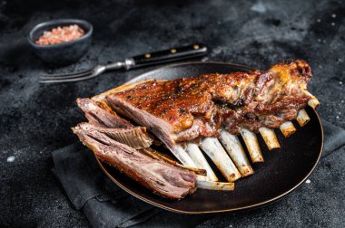 Roasted Rack of lamb ribs, mutton spareribs, sliced meat on plate. Black background. Top view.