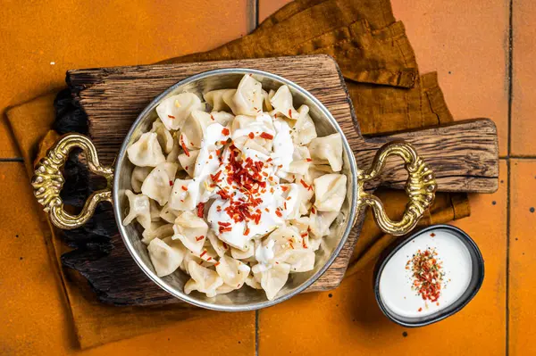 Turkish traditional manti with yoghurt and tomato sauce in a skillet. Orange background. Top view.