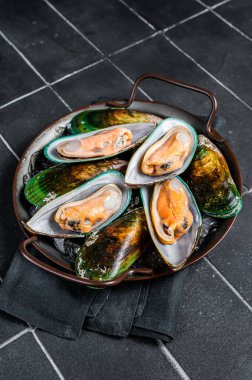 Large green mussels in shells on tray with ice. Black background. Top view.