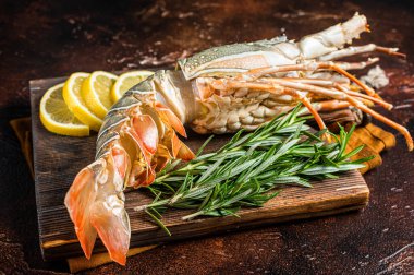 Fresh Spiny lobster on a wooden cutting board with herbs for cooking, raw seafood. Dark background. Top view.