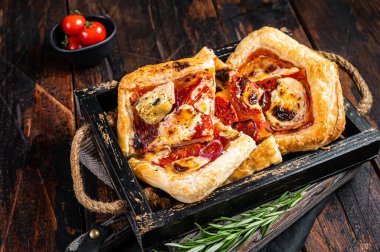 Puff pastry tart pizza with artichoke, mozzarella, tomatoes and cheese sliced in a wooden tray. Wooden background. Top view.