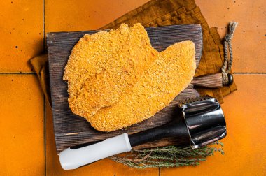 Raw Wiener Schnitzel breaded meat steak. Orange background. Top view.