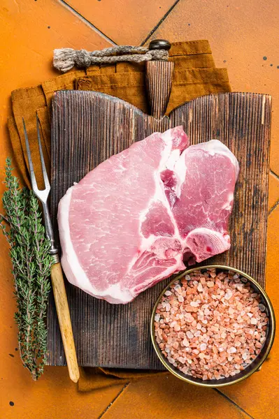 Fresh Raw pork t-bone chop meat steak on cutting board. Orange background. Top view.