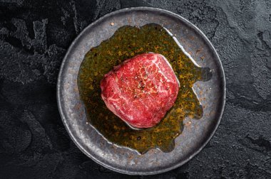 Fillet Mignon prime beef steak, raw dry aged marble meat with herbs and spices ready for cooking. Black background. Top view.