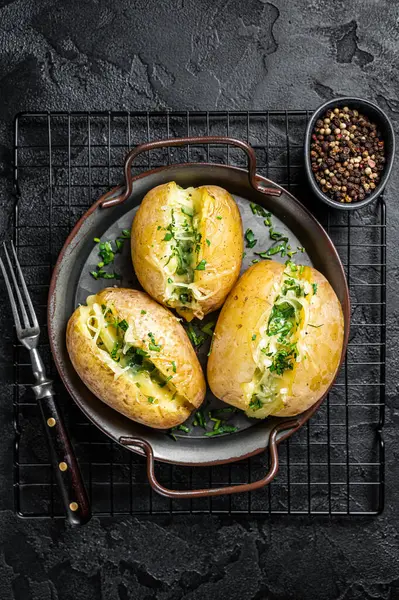 Baked Jacket potatoes with cheese, herbs and butter. Black background. Top view.