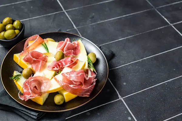 Prosciutto ham and melon salad in a plate. Black background. Top view. Copy space.