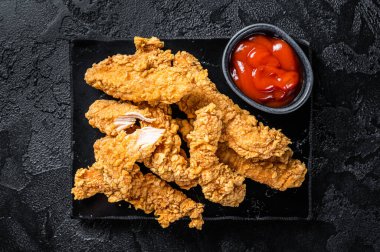Breaded chicken strips Fingers with Ketchup. Black background. Top view.