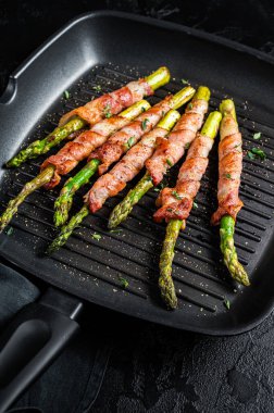 Fried bacon wrapped asparagus in a grill skillet. Black background. Top view.