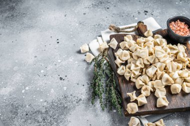 Uncooked Manti Dumpling on wooden board with herbs, raw food. Gray background. Top view. Copy space.