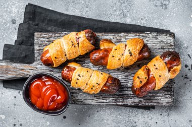 Sausage rolls, Pigs in Blanket puff pastry on wooden board. Gray background. Top view.