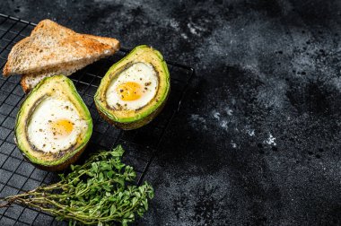 Cooking Baked Avocado with Egg. Black background. Top view. Copy space.