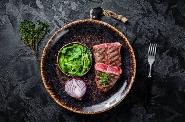 Grilled Oyster Top Blade beef meat steak on a plate with salad. Black background. Top View.