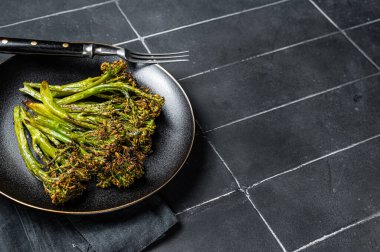 Roasted green Broccolini Sprouts with garlic butter in a plate. Black background. Top view. Copy space.