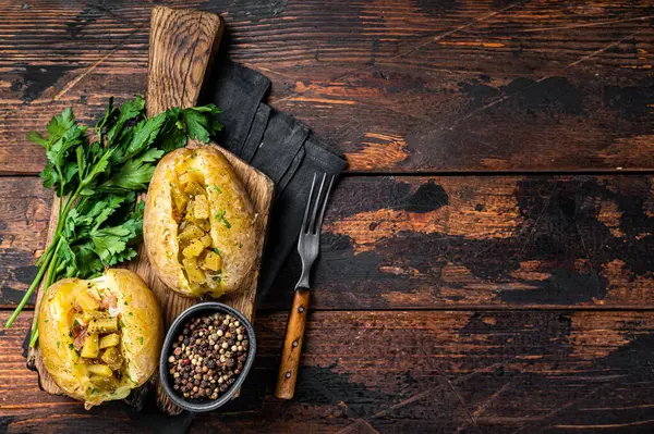 Kumpir, baked Jacket potatoes stuffed with cheese, bacon, salty cucumber, herbs and butter. Wooden background. Top view. Copy space.