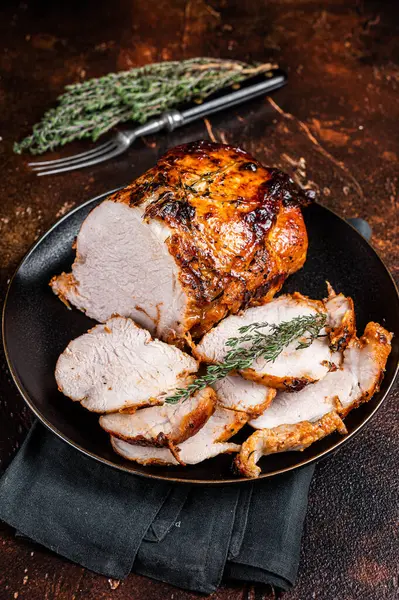 Roast rolled pork ham meat on plate with thyme. Dark background. Top view.