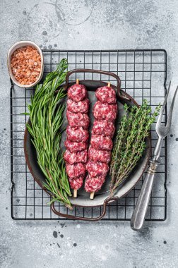 Raw Turkish Urfa kebab decorated with herbs, spices and meat fork. Gray background. Top view.