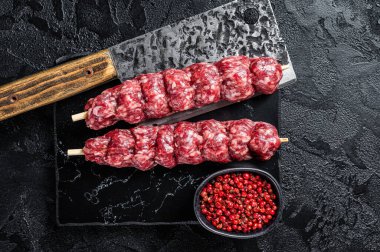 Raw beef Kofta kebab Skewers on a meat cleaver. Black background. Top view.