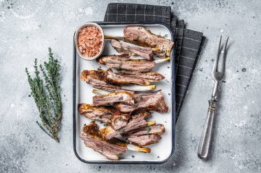 BBQ smoked lamb ribs, mutton spareribs, sliced meat in steel tray with herbs. Gray background. Top view.
