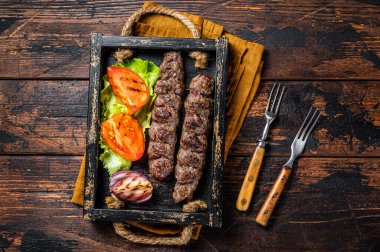 Traditional middle east kefta or kofta kebab, ground beef and lamb meat grilled on skewers served with tomato, salad and onion. Wooden background. Top view.