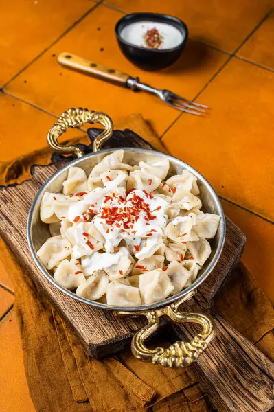 Turkish traditional manti with yoghurt and tomato sauce in a skillet. Orange background. Top view.