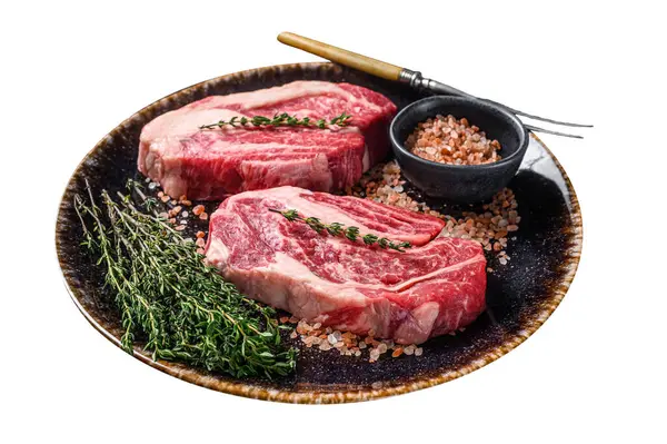 Chuck eye Roll beef steaks, raw meat on a plate with thyme and herbs. Isolated on white background. Top view