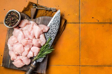 Diced sliced fresh raw chicken meat fillets, uncooked fowl. Orange background. Top view. Copy space.