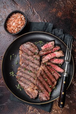 Barbecue denver strip beef meat steak on a plate. Dark background. Top view.