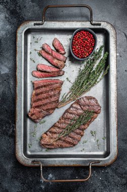 BBQ roast denver top blade beef meat steak on a steel tray with herbs. Black background. Top view.