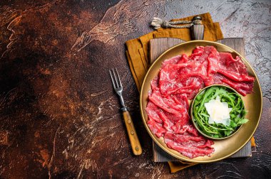 Carpaccio Beef meat appetizer with parmesan and arugula. Dark background. Top view. Copy space.