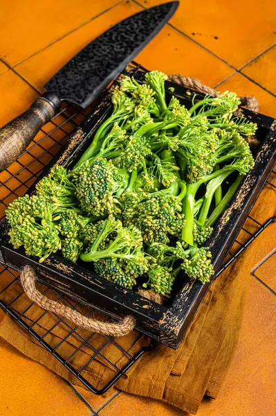 stock image Raw green baby Broccolini in a wooden tray. Orange background. Top view.