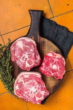 Raw lamb neck chops, fresh mutton meat on a butcher board with herbs. Orange background. Top view.
