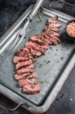 BBQ Roast sliced Skirt beef meat steak in steel tray with thyme. Black background. Top view.