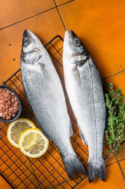 Raw Sea Bass fish with lime and herbs. Orange background. Top view.