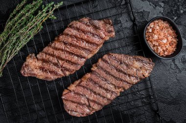 Grilled denver beef meat steak on a rack. Black background. Top view.