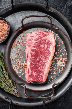 Fresh Raw Wagyu striploin or New york steak in a steel tray with herbs. Black background. Top view.