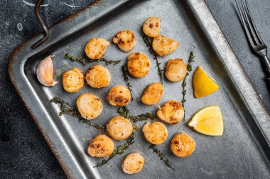 Scallops poached in a butter and garlic Sauce in a steel tray with thyme. Black background. Top view.