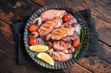 Grilled squid, calamary in a plate with herbs. Wooden background. Top view.