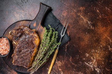 Striploin bifteği ya da ahşap bir tahtanın üzerinde otlu biftek kızartması. Karanlık arka plan. Üst Manzara. Boşluğu kopyala.