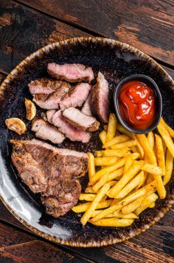 Roast BBQ pork chop steak on plate with potato chips. Wooden background. Top view.