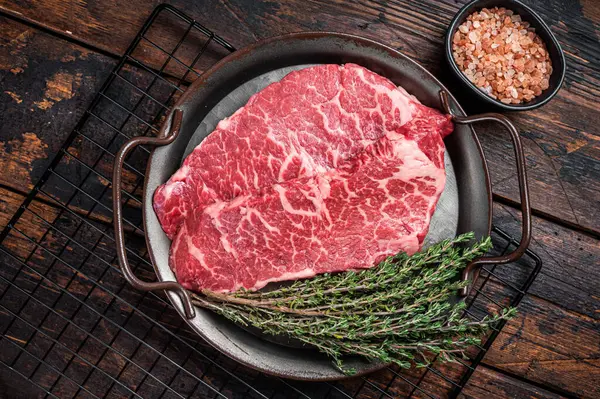 Fresh raw Denver Steak, beef meat with sea salt, seasonings and spices, ready to grill. Wooden background. Top view.