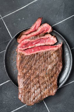 Grilled Flap or Flank Steak, sliced on a plate. Black background. Top view.